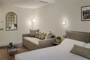 Quarto de hotel moderno com uma cama, um sofá, uma pequena mesa com uma planta e um espelho fixado na parede.
