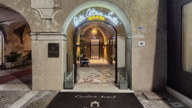 Entrada do Porta Altina Suites, com piso xadrez e um letreiro de neon acima.