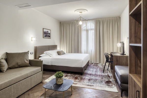 Quarto de hotel moderno com cama, sofá, escrivaninha e uma pequena mesa com uma planta.