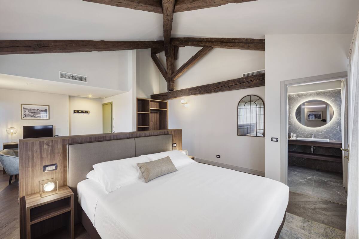 A modern bedroom with a large bed, wooden beams, a built-in wardrobe, and a bathroom with a marble sink.