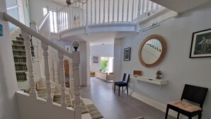 Amplia sala de estar con una escalera blanca, un espejo redondo y un tapete estampado.