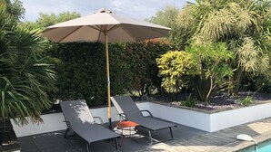 Zona de piscina al aire libre con dos sillones de relax y una sombrilla grande.