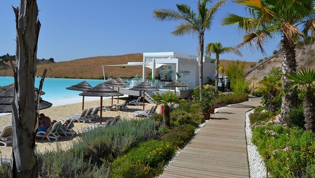Un complexe hôtelier de bord de mer doté de chaises longues, de parasols, d’une piscine et d’une promenade en bois.