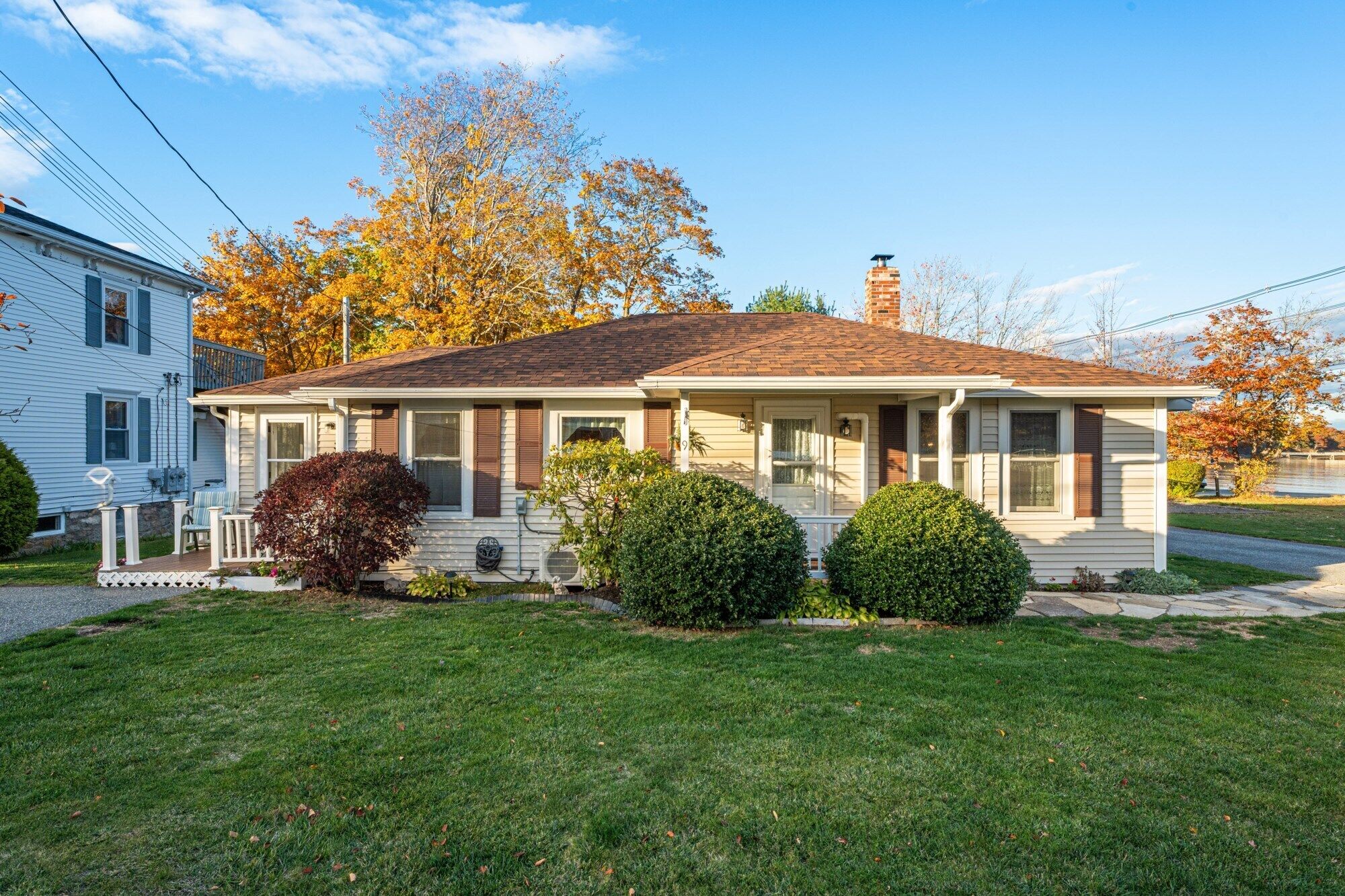 A single-story house with a porch, a chimney, and a small front yard with two bushes.