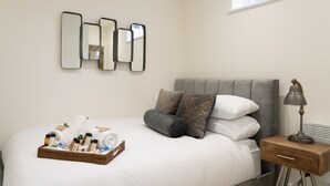 Una cama bien hecha con un tray de artículos de aseo, una lámpara de noche y una ventana con persianas.