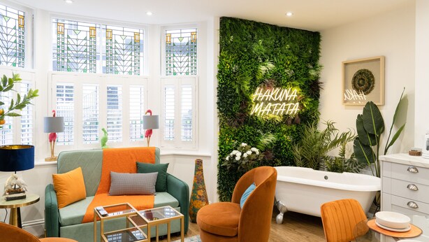 Una sala de estar moderna con un sofá verde, sillones naranjas, una mesa de centro de vidrio y un ventanal con vitrales.