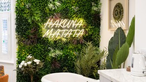 Un baño con pared verde, un letrero de neón, una bañera con bolas de colores y un lavamanos blanco.