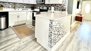 A modern kitchen with white cabinets, a central island, a microwave, and a stainless steel sink. - Spacious & Luxurious Villa - Large Fenced Backyard (West Palm Beach)
