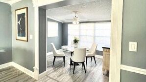 A spacious room with a dining area featuring a round table and four chairs, a ceiling fan, and a view through an open doorway. - Spacious & Luxurious Villa - Large Fenced Backyard (West Palm Beach)