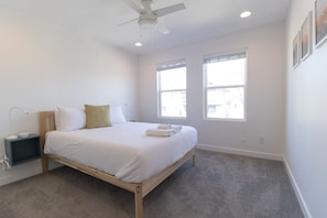 A bedroom with a bed, a ceiling fan, two windows, and a nightstand.