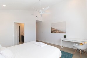 A modern bedroom with a bed, a desk, and a ceiling fan.
