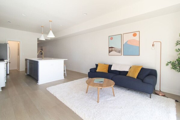 Una sala de estar moderna con un sofá, una mesa de centro y una zona de cocina al fondo.