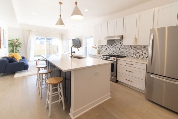 A modern kitchen with white cabinets, a stainless steel refrigerator, and a central island with stools.