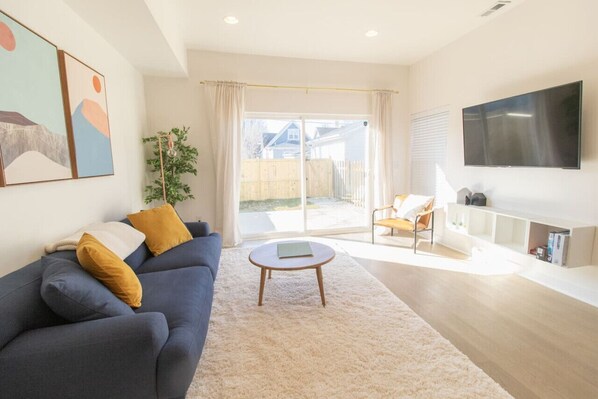Relax in this stylish living room with a sofa, coffee table, and flat-screen TV, leading to an outdoor area through a sliding glass door.