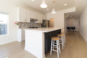 Una cocina moderna con armarios blancos, una isla grande con taburetes y un salpicadero con diseño.
