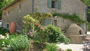 Una casa de piedra con jardín, horno de piedra y mobiliario exterior.