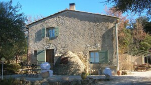 Una casa de piedra con dos ventanas, una chimenea y un camino de entrada de grava.