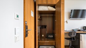 Une pièce de taille modeste comprenant un lit, un bureau, une chaise, un téléviseur et un petit réfrigérateur.