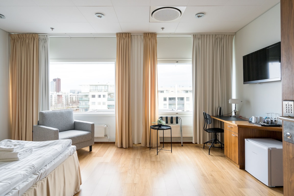 Ein Hotelzimmer mit Bett, Schreibtisch, Stuhl, kleinem Kühlschrank und Fernseher.