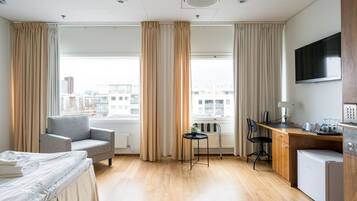 A hotel room with a bed, a desk, a chair, a small fridge, and a TV.
