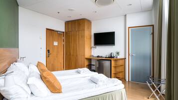 Hotellihuone, jossa on kaksi sänkyä, taulutelevisio, työpöytä tietokoneella sekä pieni keittokomero.