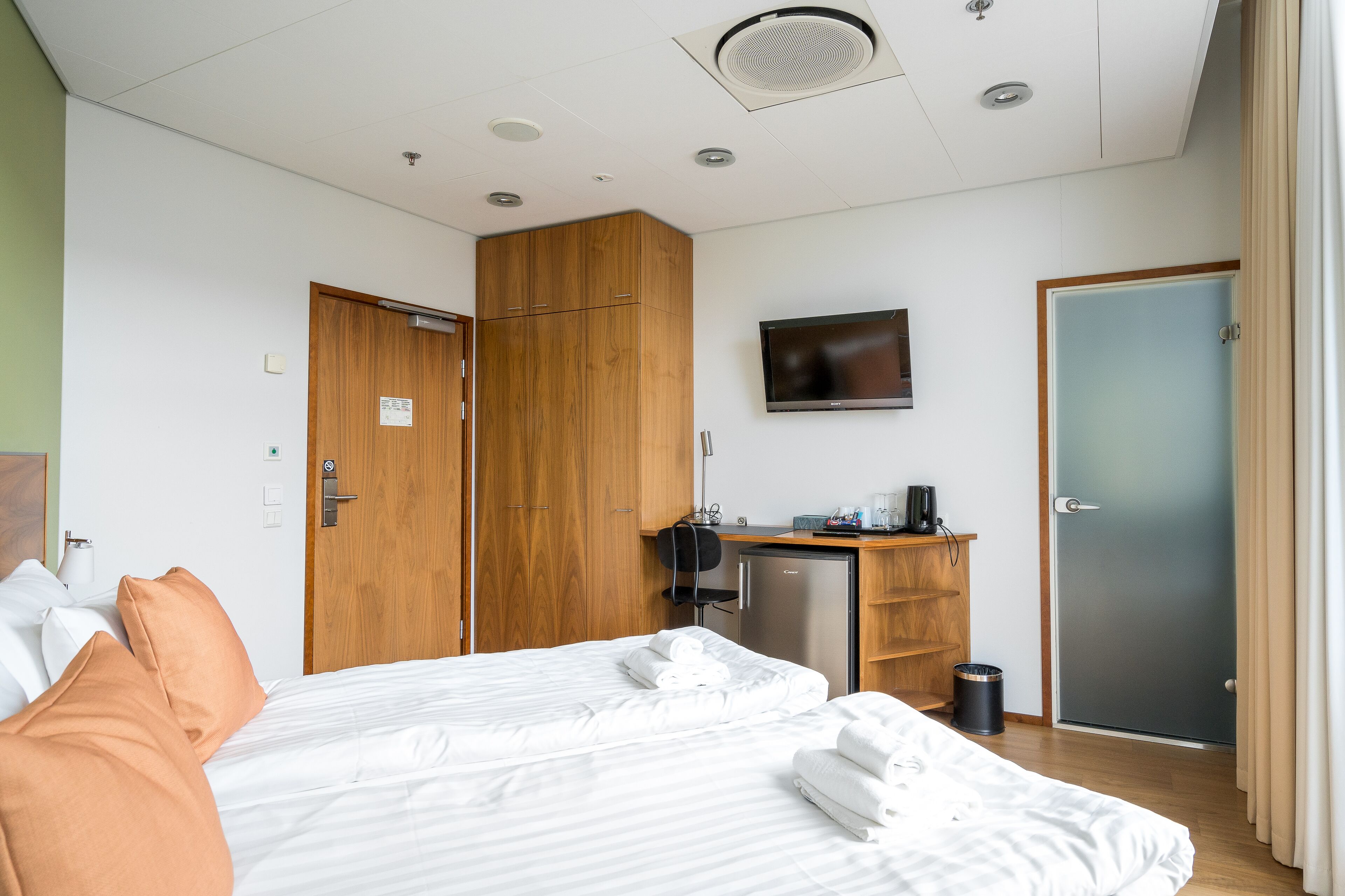 A hotel room with a bed, a desk with a computer, a television, and a wardrobe.