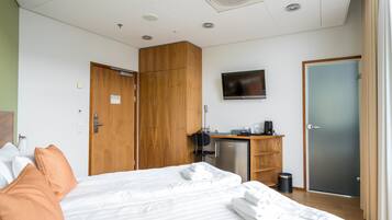 A hotel room with a bed, a desk with a computer, a television, and a wardrobe.