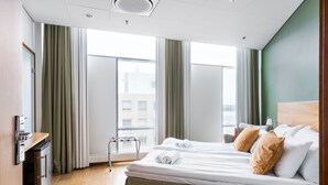 Une chambre d’hôtel avec deux lits, une kitchenette et de grandes fenêtres équipées de rideaux.