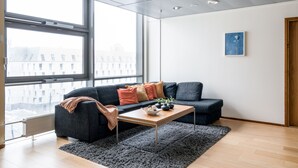 Un salon moderne avec un canapé gris, une table basse en bois et une vue sur un paysage urbain enneigé, visible à travers de grandes fenêtres.