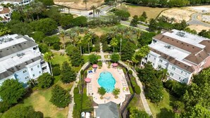 An aerial view of a residential area with a central swimming pool surrounded by a fence, adjacent to multi-story buildings. - 3BR Golf View w/ $50 Theme Park Credit (Kissimmee)