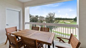 A balcony with a wooden table and chairs, a white door, and a view of a golf course. - 3BR Golf View w/ $50 Theme Park Credit (Kissimmee)