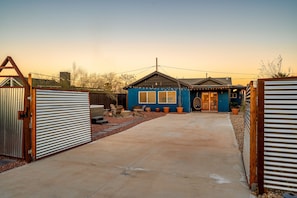 A blue house with a covered patio, a fenced yard, and a clear sky.
