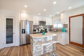 A modern kitchen with a central island, stainless steel appliances, and a stone backsplash.