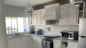 Una cocina moderna con armarios blancos, electrodomésticos de acero inoxidable e iluminación colgante.