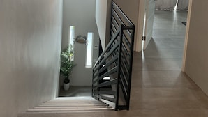 Una escalera con barandilla metálica, una lámpara colgante y una planta en maceta.