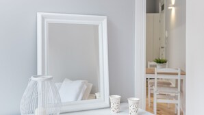 Un miroir à cadre blanc, posé sur une table blanche, avec un vase blanc et deux tasses blanches.