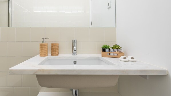 A bathroom with a white sink, a mirror, and a wooden storage unit with plants.