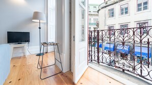 Une pièce avec un téléviseur posé sur un meuble, un lampadaire et un balcon agrémenté de balustrades en métal ouvragé.