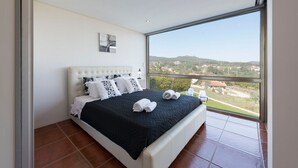 Une chambre avec une grande fenêtre, un lit avec une literie noire et blanche, et une vue sur un paysage vallonné.