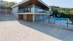 Une maison moderne à deux étages, dotée d’un balcon, d’une piscine et d’un mur en pierre.