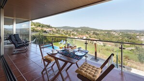Un balcon avec une table dressée pour le petit-déjeuner, offrant une vue panoramique sur un paysage vallonné.