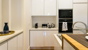 A modern kitchen with white cabinetry, a black microwave, an oven, and a kettle on the countertop.
