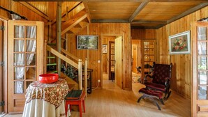 Interior de madera con una escalera, un cuenco rojo sobre una mesa, una silla roja y un cuadro en la pared.