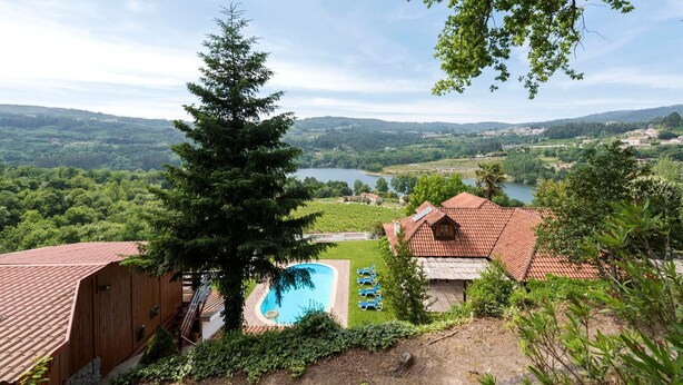 Una villa con piscina, rodeada de vegetación exuberante y vistas a un lago y colinas.