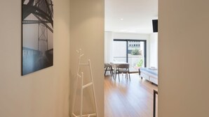 Un interno moderno con una parete bianca, una scala, un'area pranzo con tavolo e sedie, e un'ampia finestra vista su edifici e vegetazione.