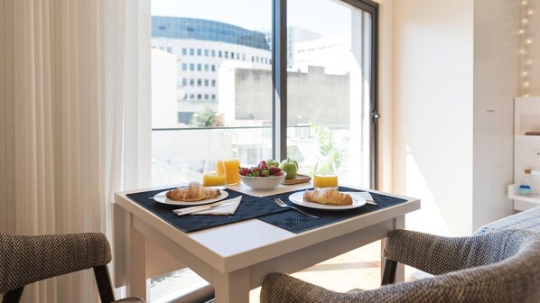 A breakfast table with croissants, fruit, and orange juice in a bright room with a view of buildings.