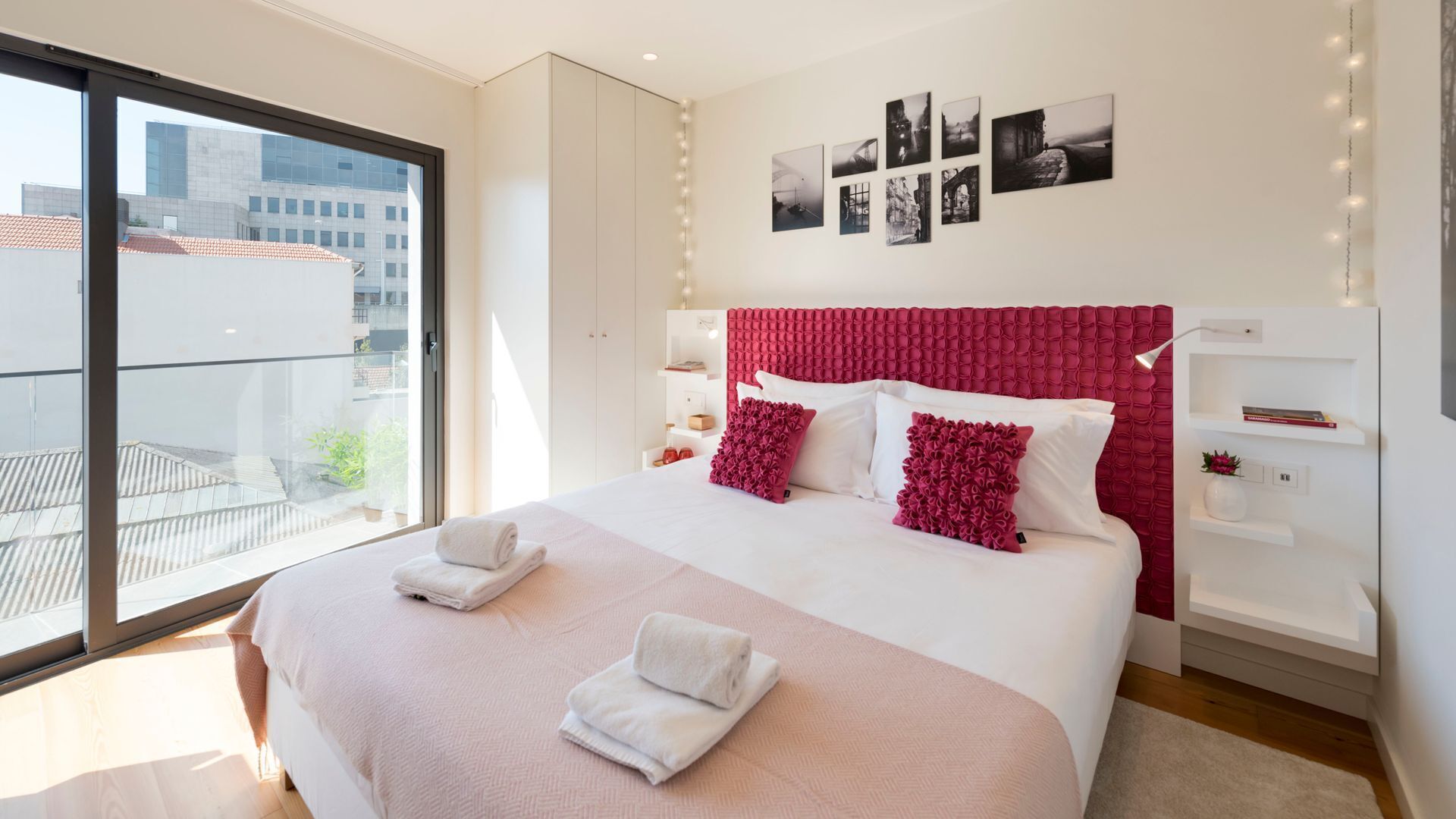 Habitació d'hotel moderna amb un llit gran, un balcó i vistes a la ciutat, i una paret amb quadres emmarcades.