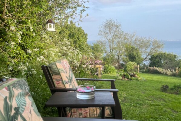A garden with a table and chair, a birdhouse, and a view of the sea.
