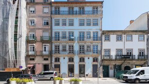 Un edificio de varios pisos con balcones, vista a la calle, coches estacionados y una furgoneta.