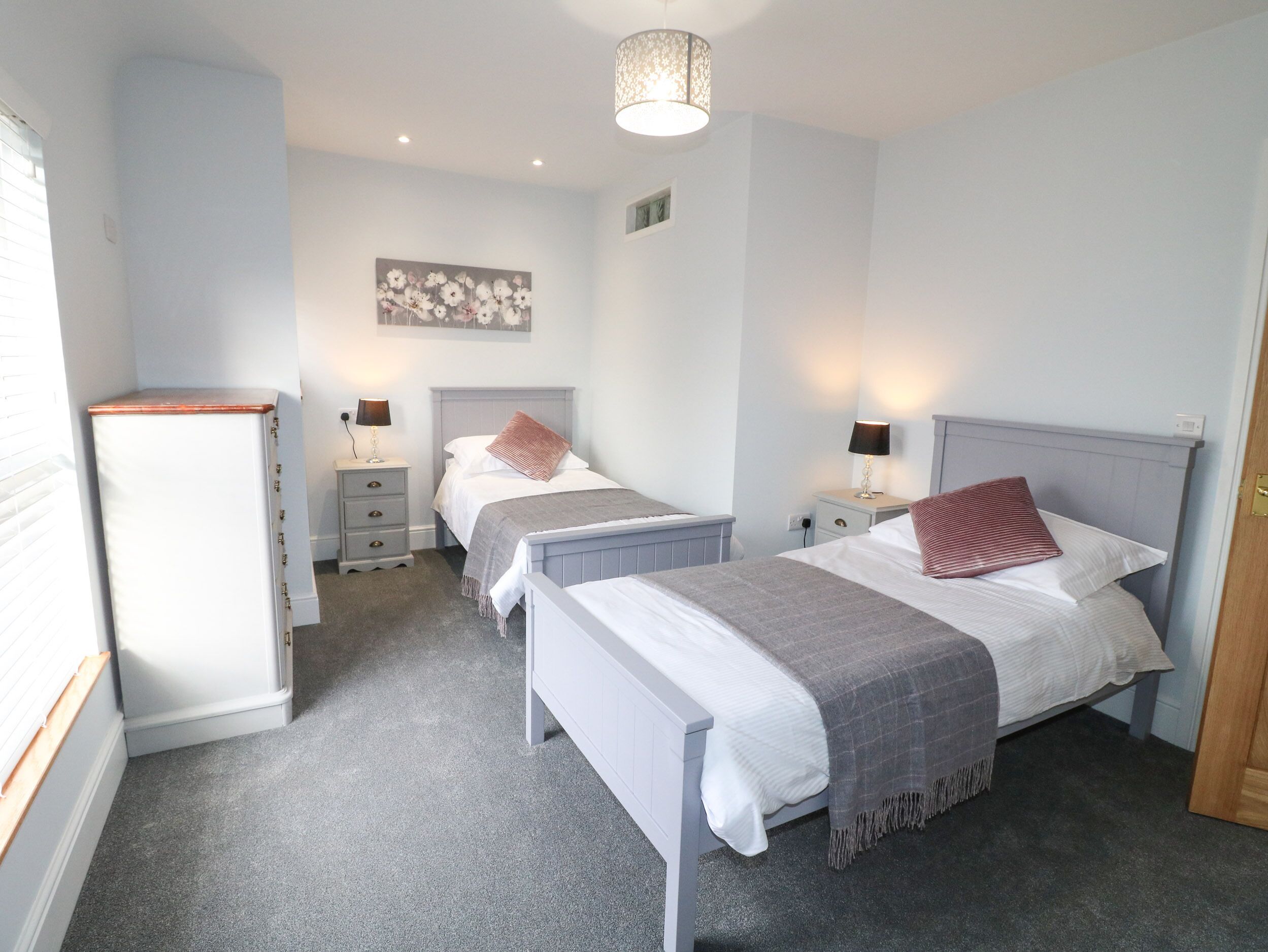 A bedroom with two single beds, a nightstand with a lamp, a dresser, and a ceiling light fixture.